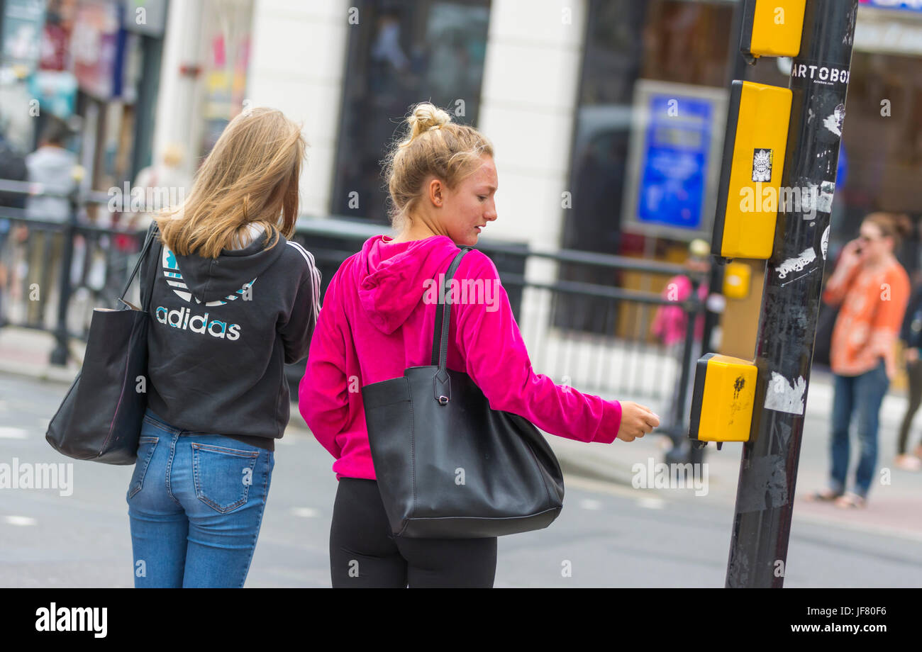 Friends waiting to cross a road at pedestrian crossing traffic lights in the UK. Stock Photo