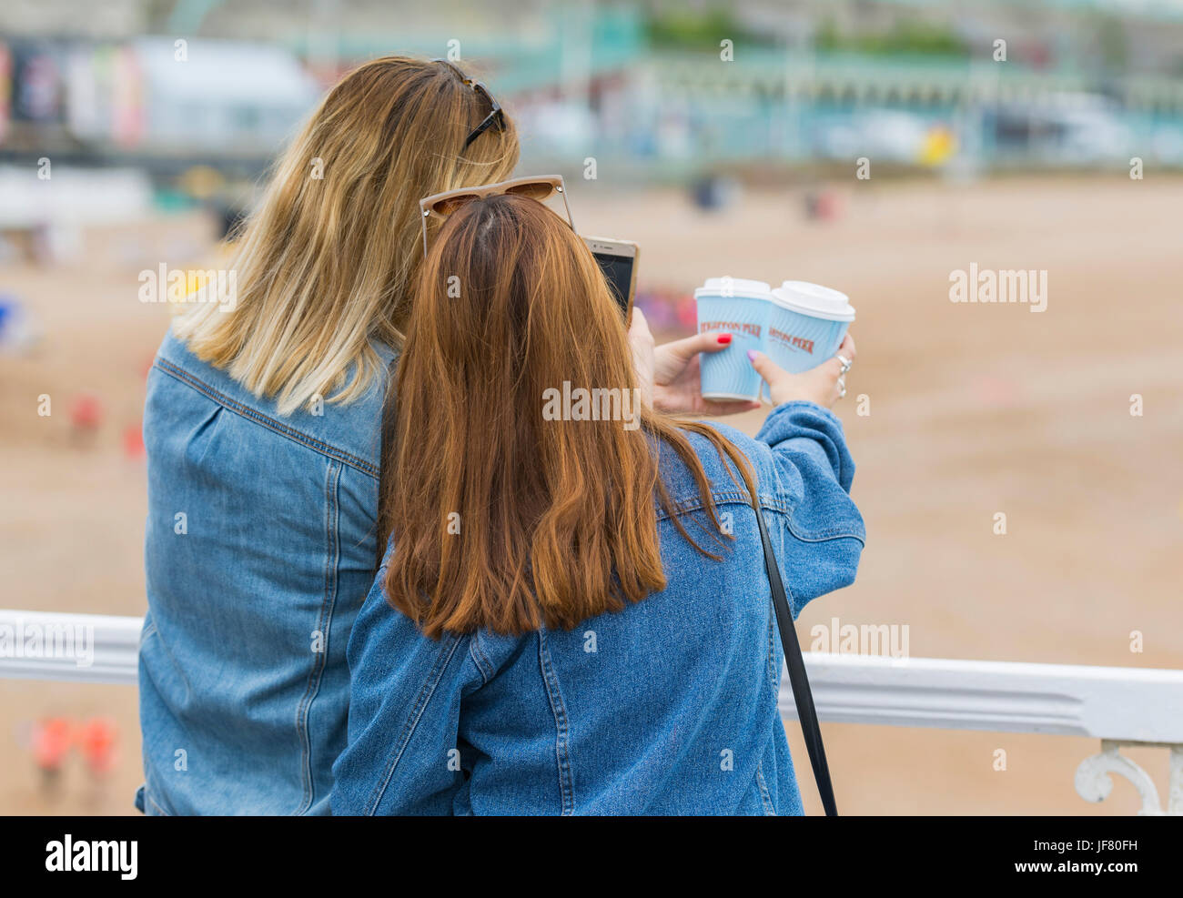 Female friends on a pier at the seaside taking photos. Stock Photo