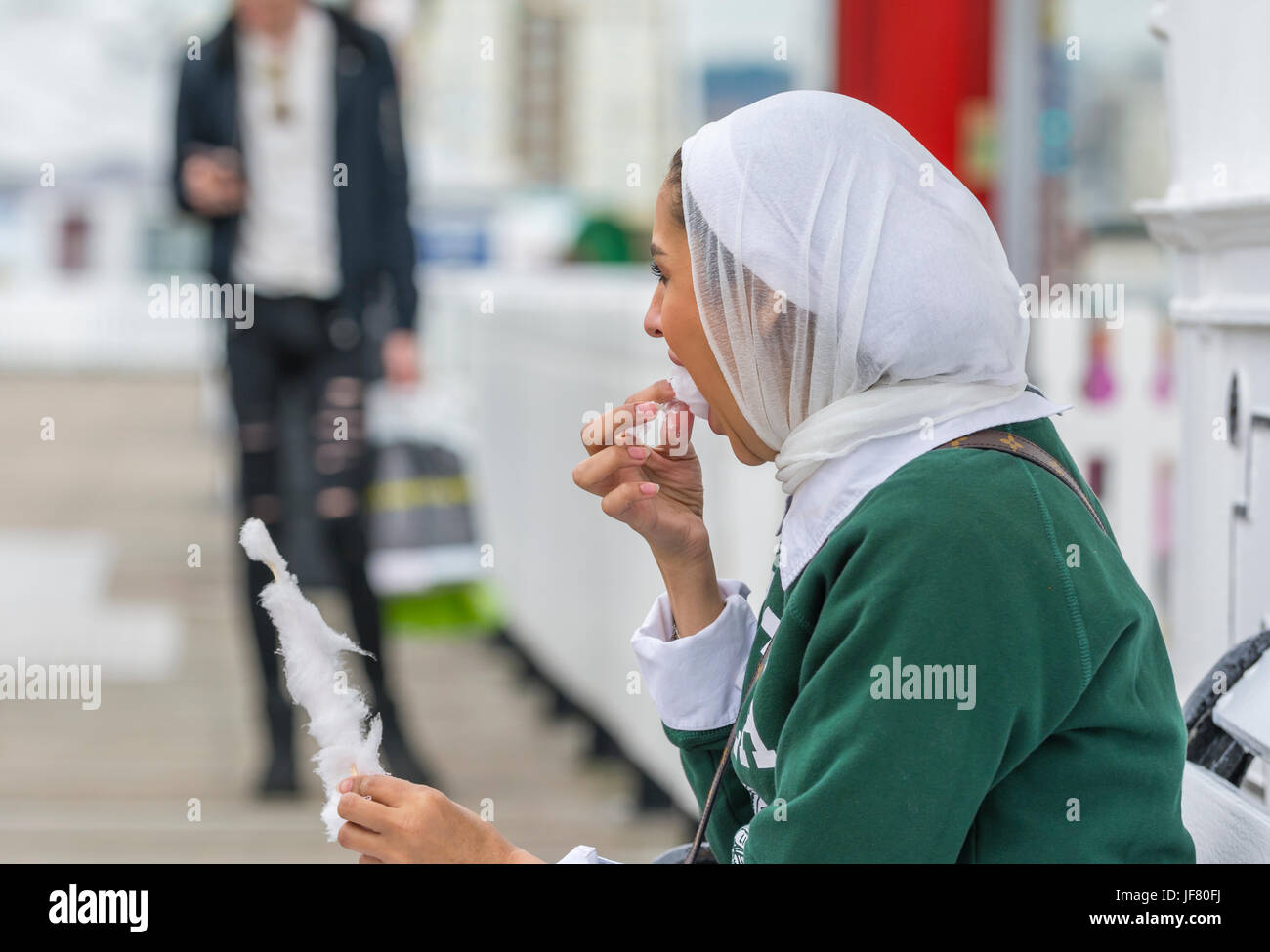 Asian woman wearing a headscarf sitting outside eating in the UK. Stock Photo