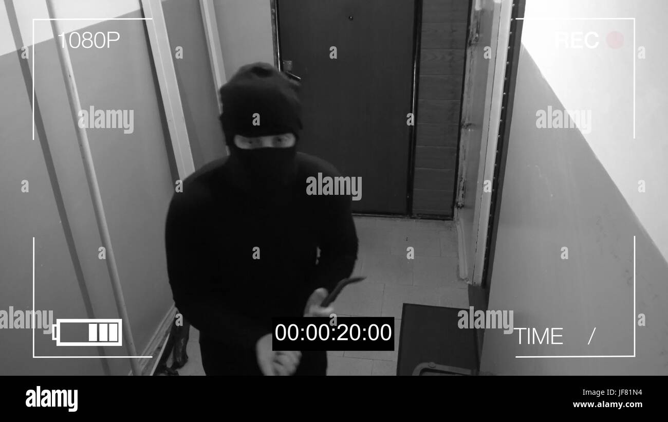 the masked robber burst through the door and broke the security camera with a tire iron. Stock Photo