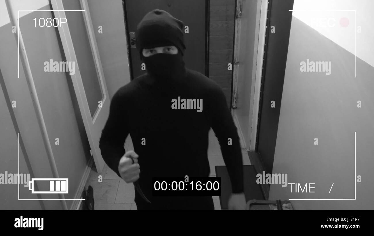 the masked robber burst through the door and threatened with a knife in CCTV camera. Stock Photo