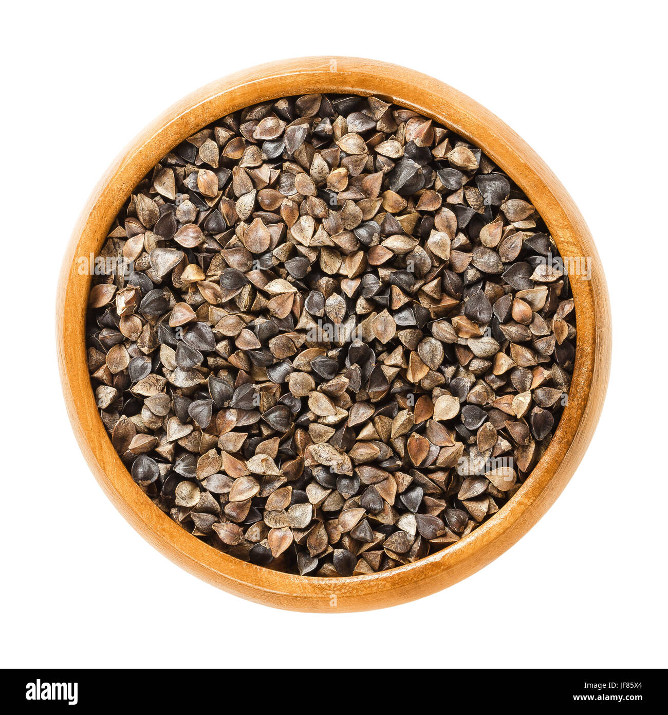 Common buckwheat seeds with hulls in wooden bowl. Fagopyrum esculentum, also Japanese or silverhull buckwheat. Gluten free pseudocereal. Dried seeds. Stock Photo