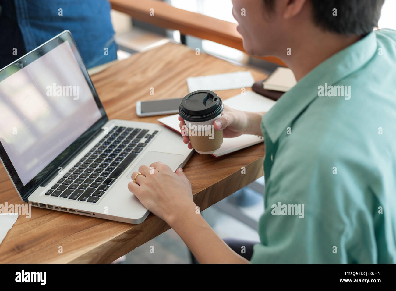 Asian hipster male with casual cloths using laptop computer touchpad while drinking coffee in cafe on workday. Freelance worker lifestyle and activity Stock Photo