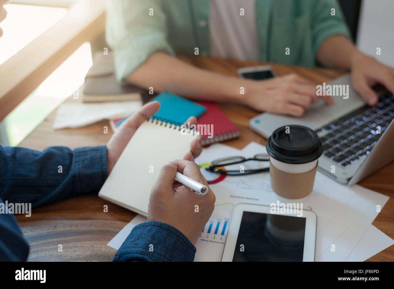 Young hipster worker writing on small notebook while meeting with colleagues in coworking space. Freelancer teamwork and brainstorm concept Stock Photo