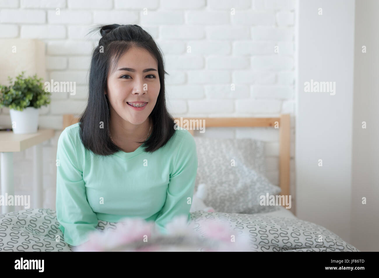 Young attractive Asian woman wear green casual cloth smiling while sitting on bed. Lazy girl activity on sunday morning. Stock Photo