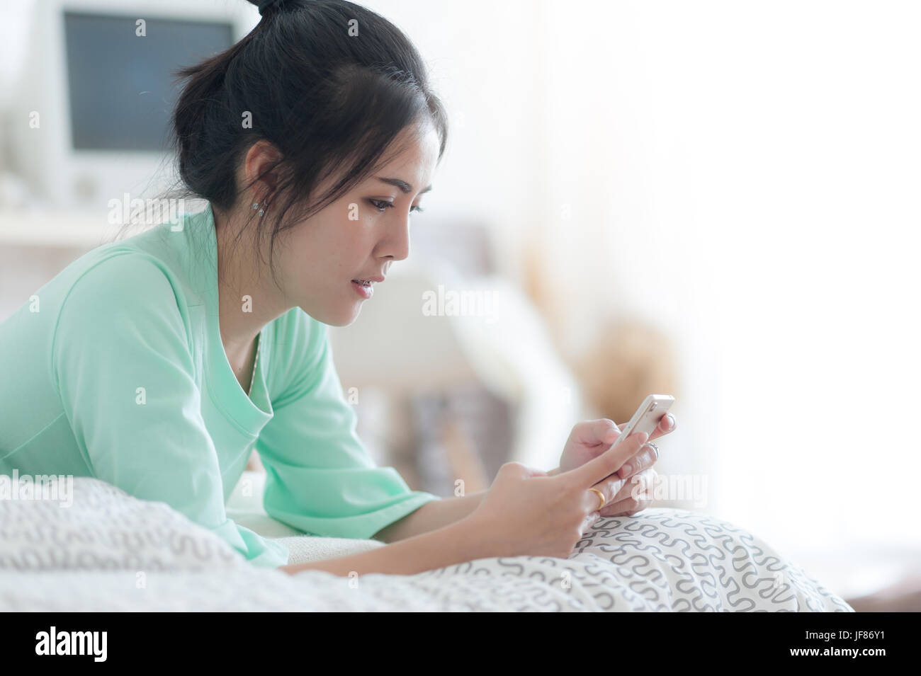 Young attractive Asian woman wear green casual cloths stretching after wake up on bed. Lazy girl activity on sunday morning. Stock Photo