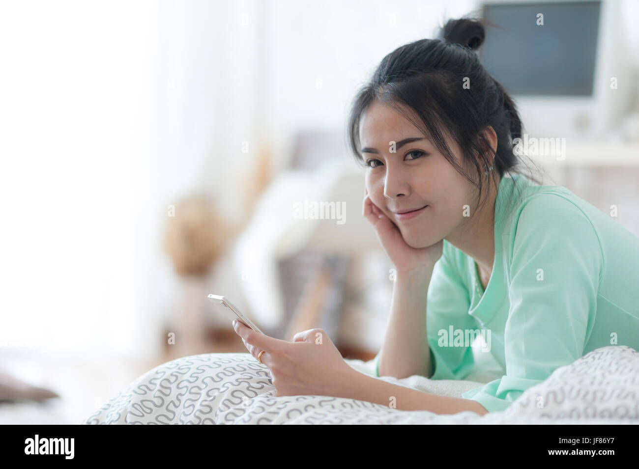 Young attractive Asian woman wear green casual cloths stretching after wake up on bed. Lazy girl activity on sunday morning. Stock Photo