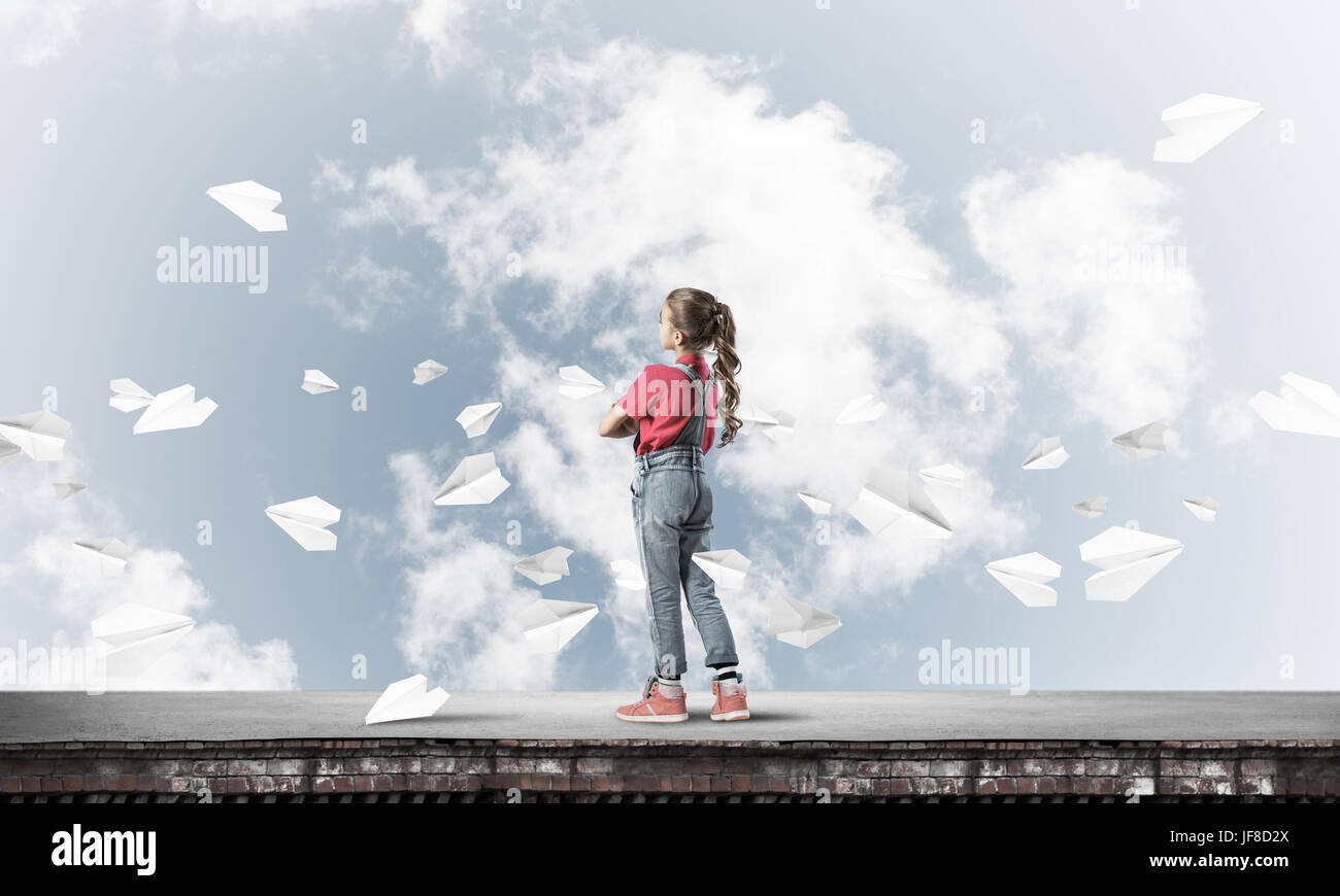 Cute kid girl standing on building roof and paper planes flying around ...