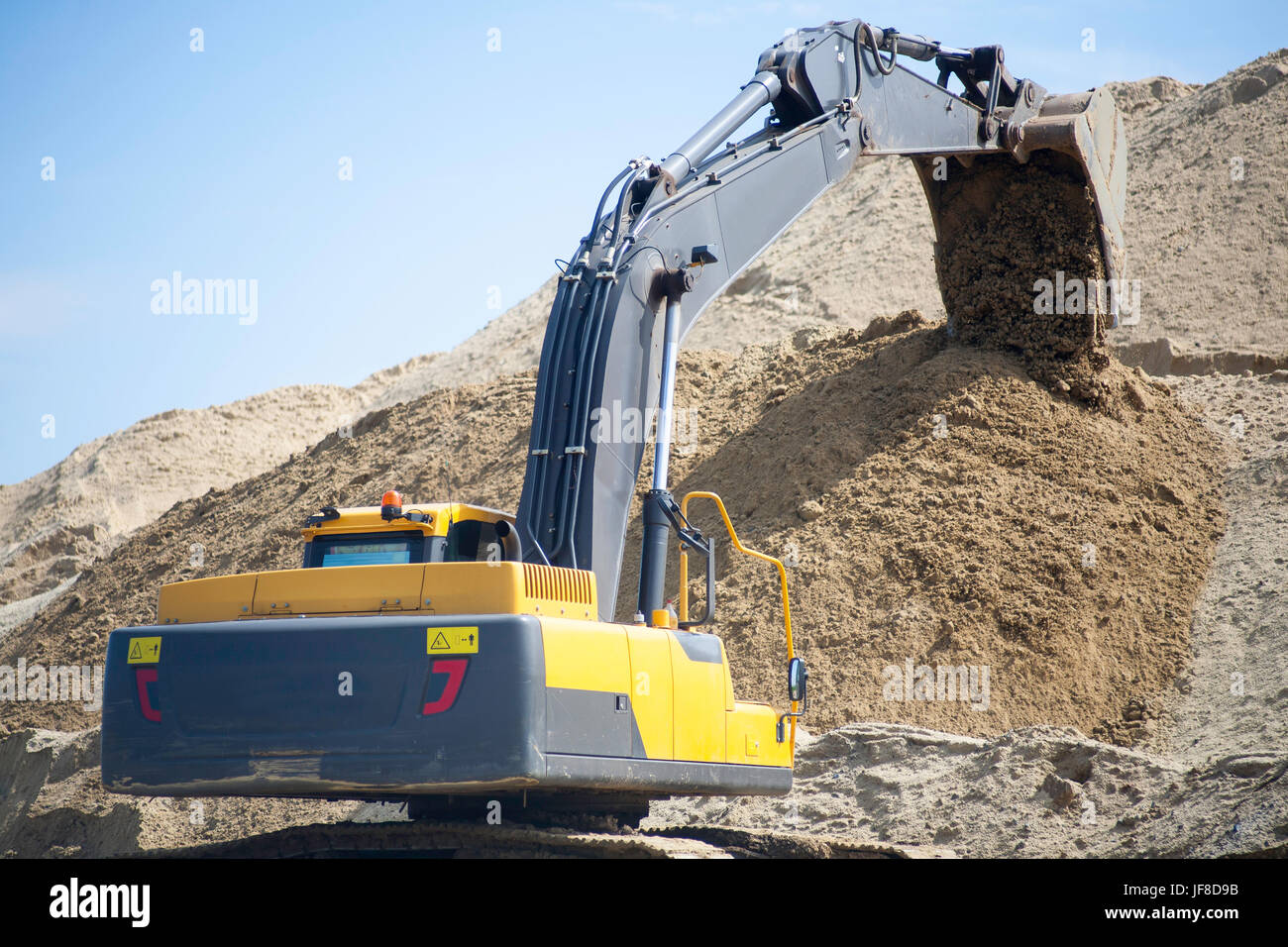 A large yellow excavator on the road construction site picks up and ...