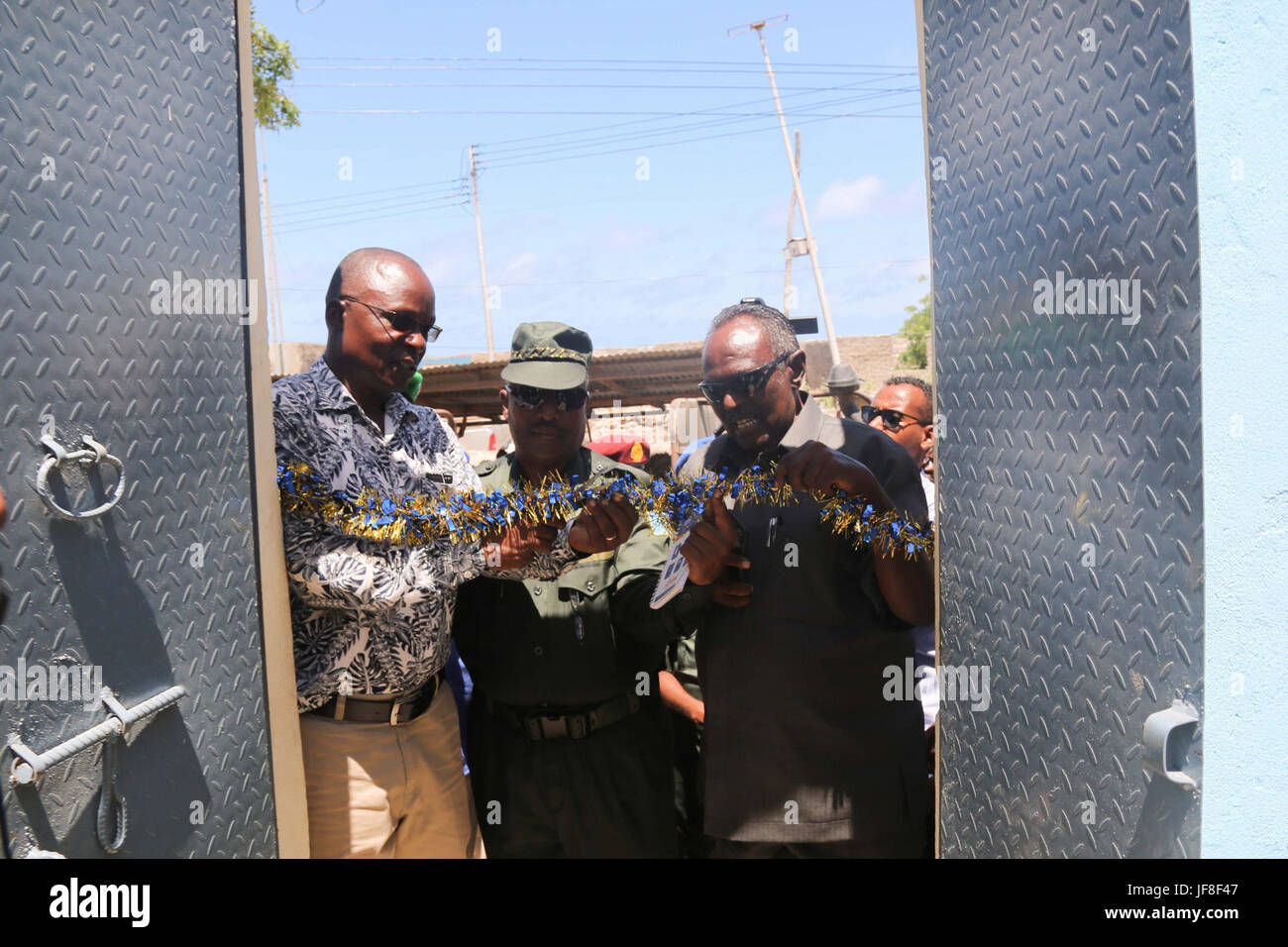 Dr. Opiyo Ododo (left), the head of stabilisation and early recovery of the African Union Mission in Somalia (AMISOM), Ahmed Nasir, the Jubbaland Police commissioner (middle), and   Ibrahim Mohamed Yusuf,  the Mayor of Kismayo (right),cut the tape to officially handover the newly renovated police station to Jubbaland Administration on May 8, 2017. AMISOM Photo Stock Photo