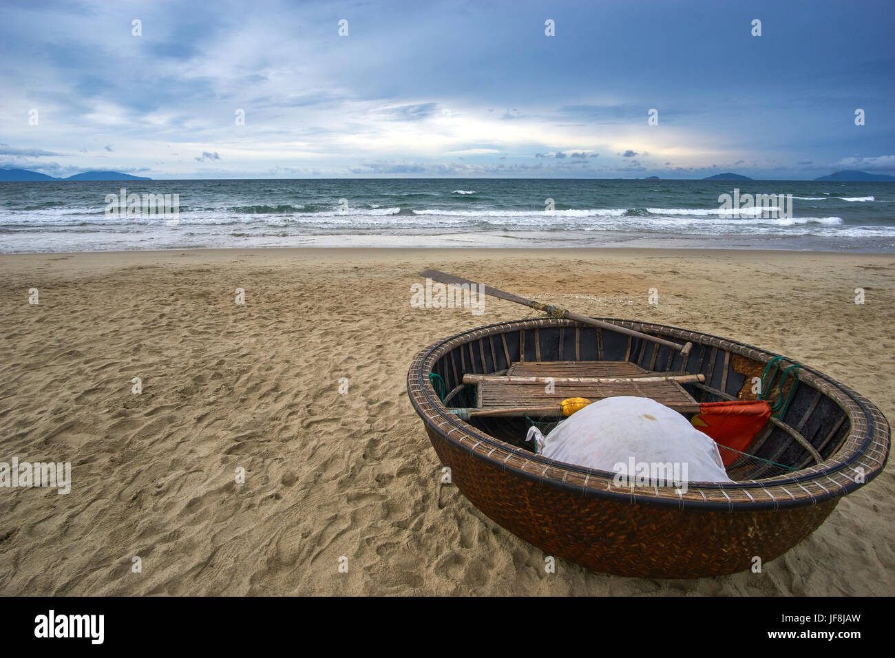Stormy evening at the beach with dramatic clouds and waves. Traditional vietnamese coconut boat in the foreground. Hoi an, An Bang beach. Stock Photo