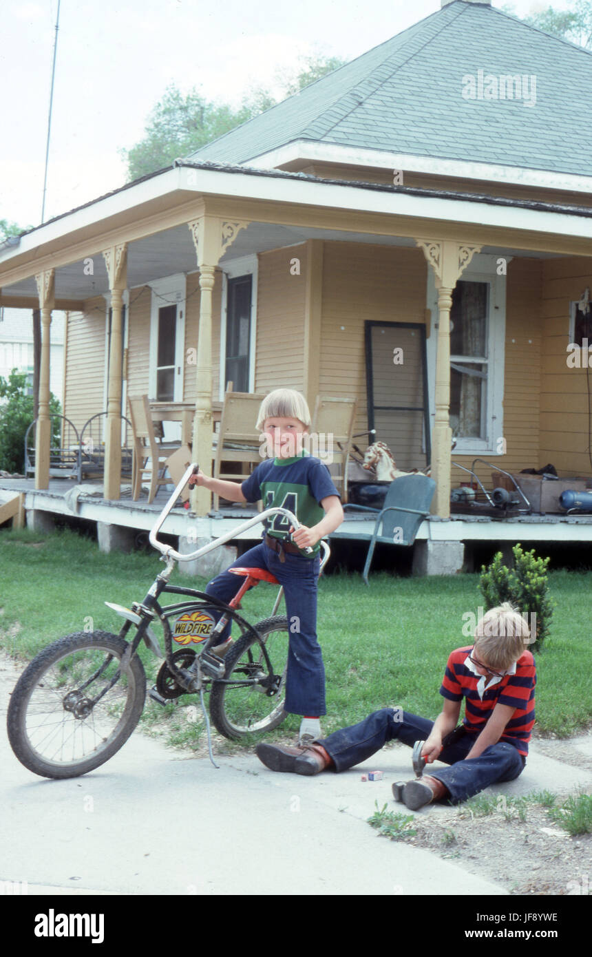 Boys together in 1970's one with a Raleigh Chopper bike standing in front of a home with no basement and a large porch in Stapleton Nebraska Stock Photo
