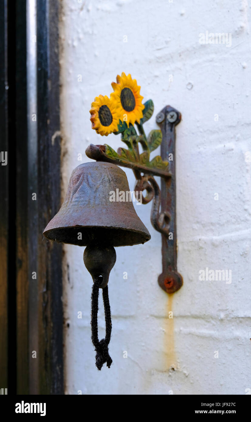 Rusting ornamental metal doorbell decorated with yellow painted sunflowers and attached to an outside wall Stock Photo