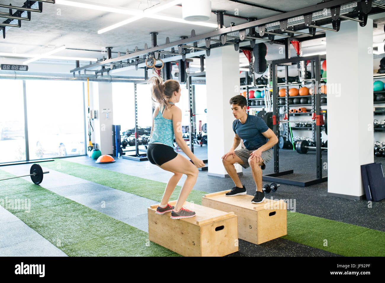 Young fit couple exercising in gym, doing box jumps. Stock Photo
