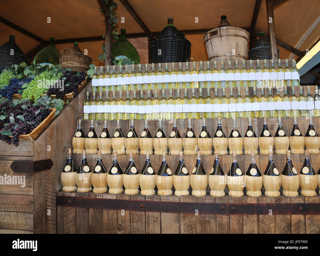 Lots of wine bottles with big carboys and grapes in the wine cellar