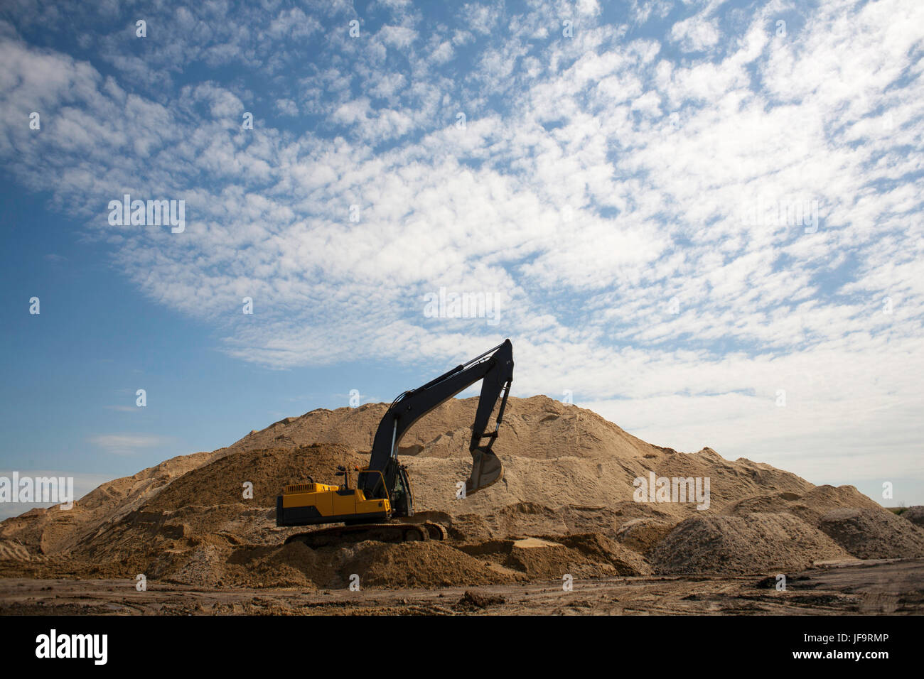 A large yellow excavator on the road construction site picks up and ...