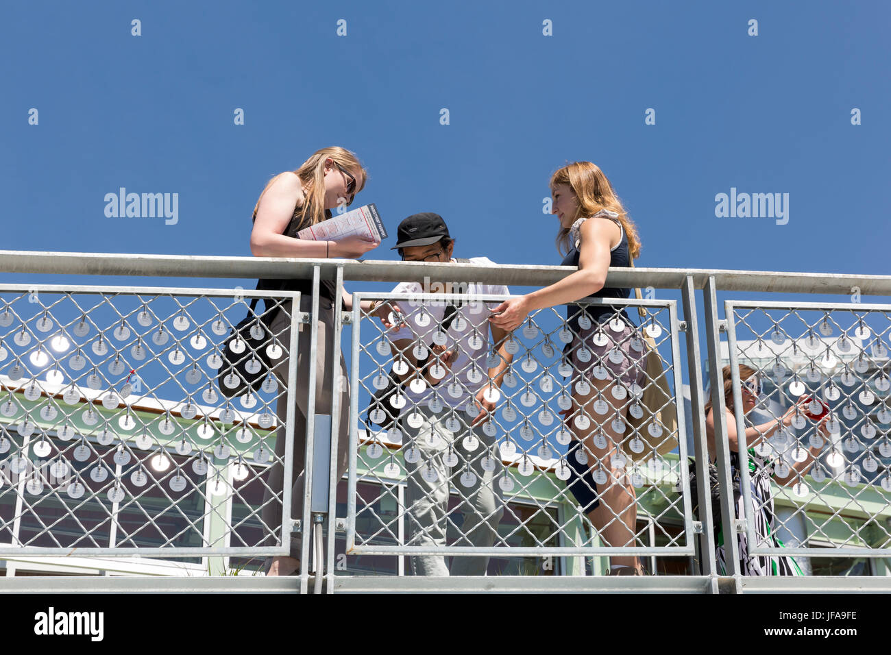 Seattle, Washington: A group of friends examine the Market Charm Fence at Pike Place MarketFront's grand opening. The charms on display as an art installation, were purchased by market supporters as part of the Market Foundation's “Pike Up!” campaign to help fund the project. The $74 million MarketFront expansion provides a dynamic public plaza with views of Puget Sound and Olympic Mountains as well as table space for farmers, craftspeople and artisan purveyors, retail space, low-income housing, a neighborhood center and parking. The project was created in accordance of Market historic distric Stock Photo