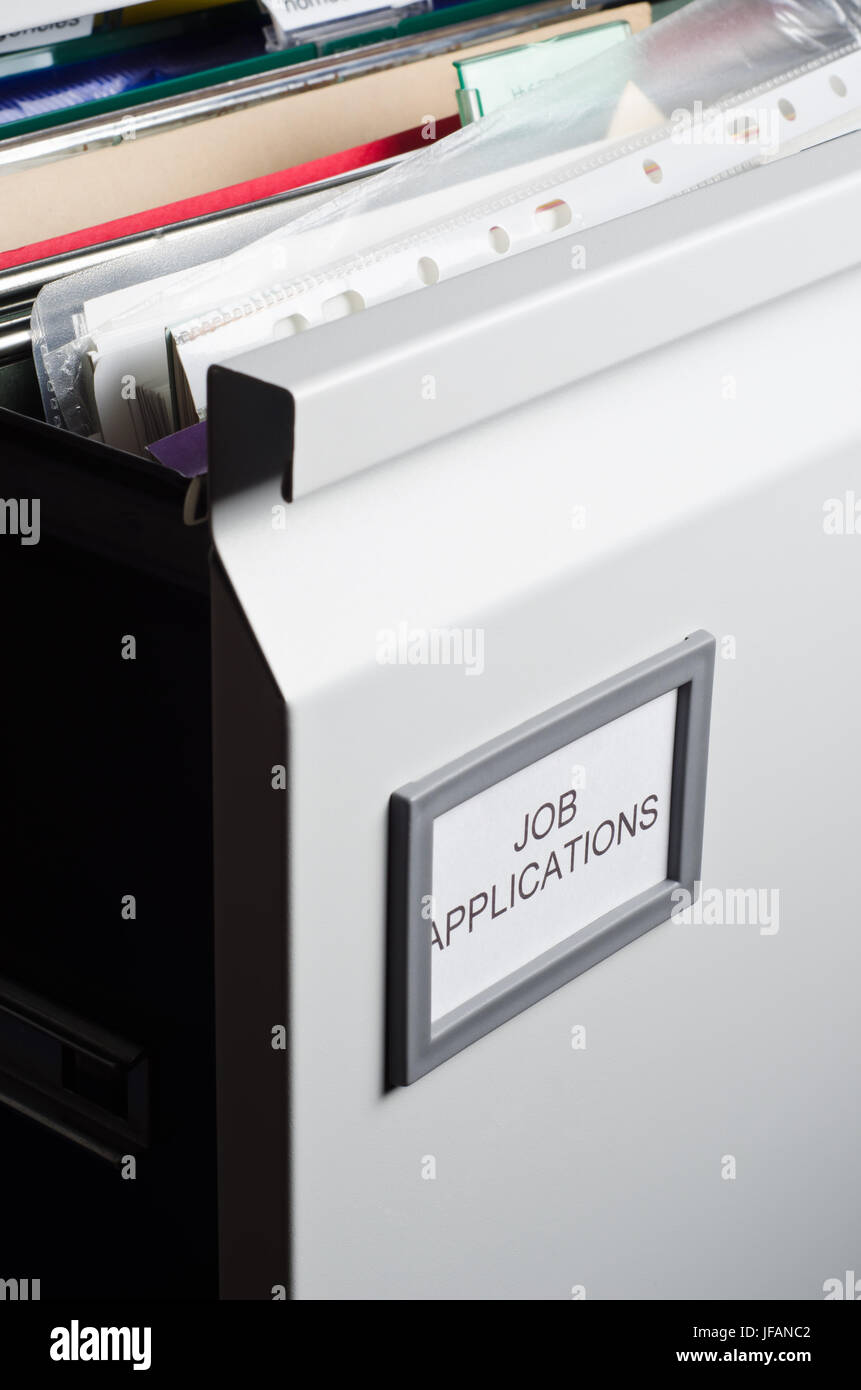 An open filing drawer, labeled 'Job Applications' and filled messily with hanging files, folders, plastic wallets and papers.  Portrait orientation. Stock Photo