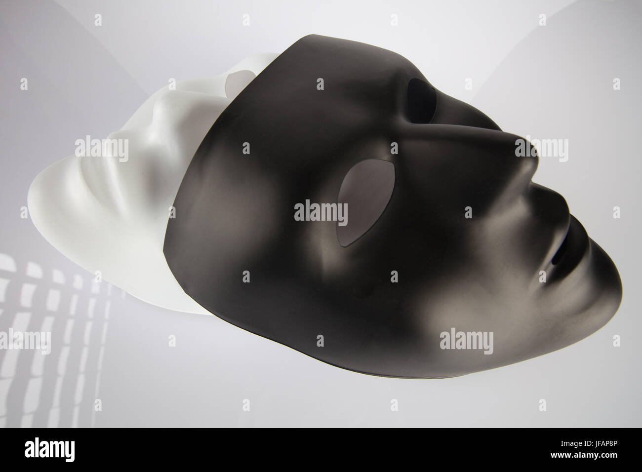 Black and white masks stacked on top of each other on white reflective surface. Identity and race concept Stock Photo
