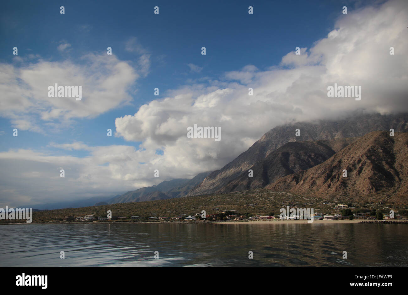 View of Los Angeles Bay in Baja California Norte from the water; topped with white clouds, blue sky, rugged mountains rise up behind the village, Stock Photo