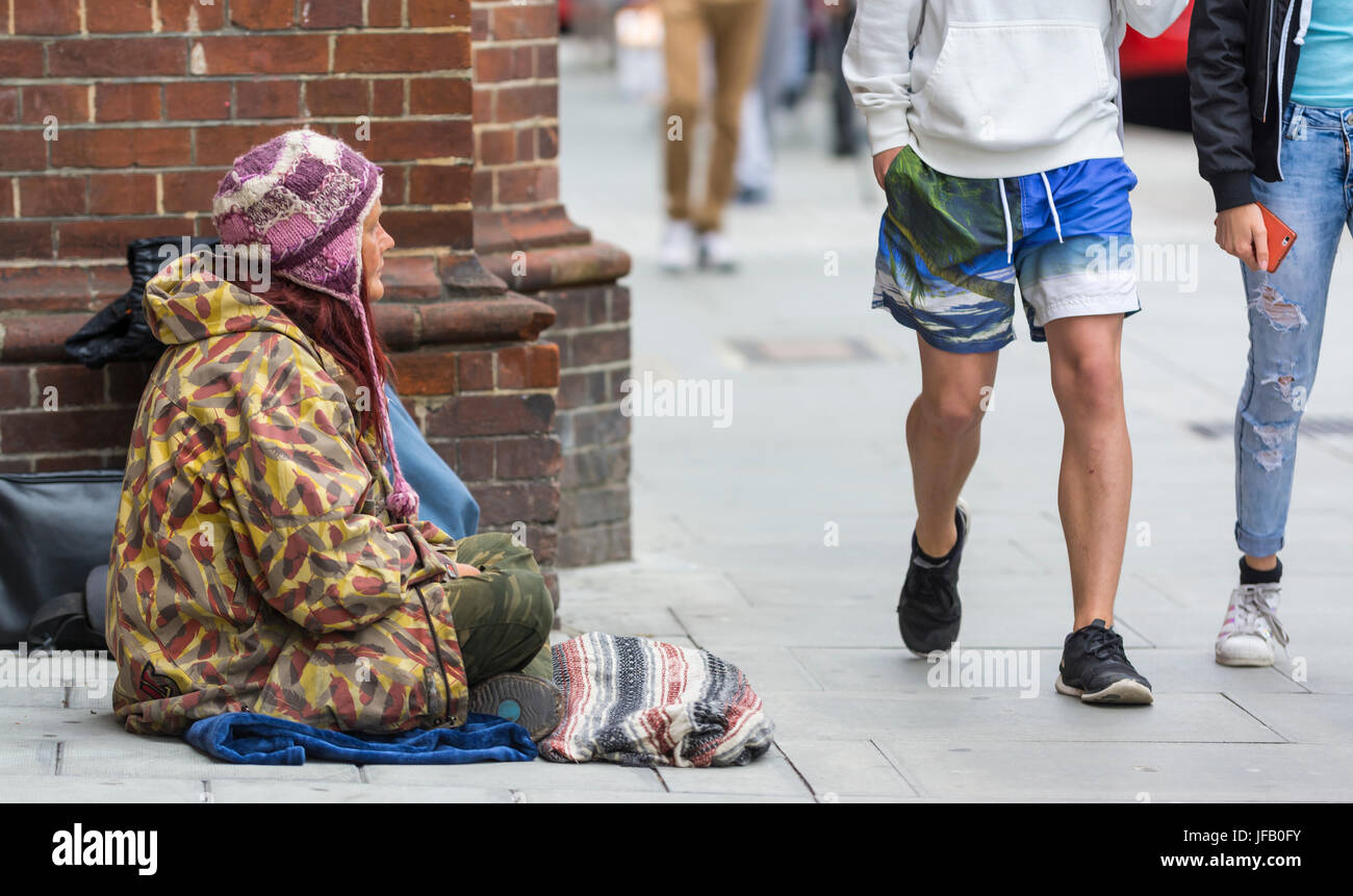 Homeless lady sitting on the ground as people walk past ignoring her. Stock Photo