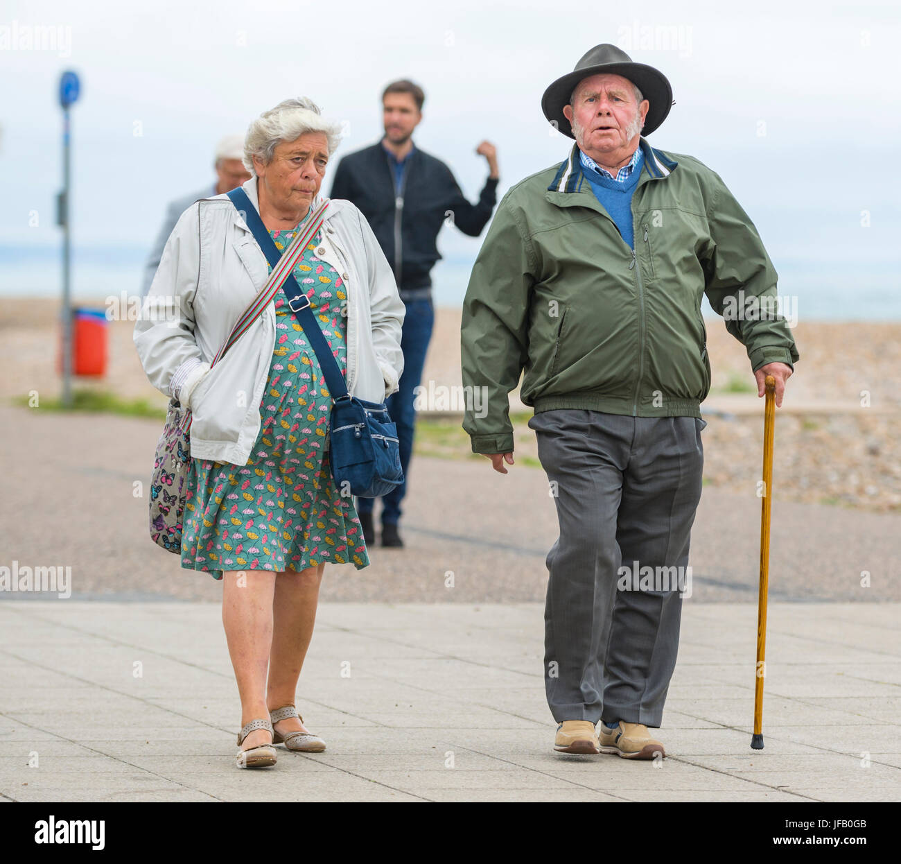 Elderly couple and man with a walking stick walking along with hat and coats. Stock Photo