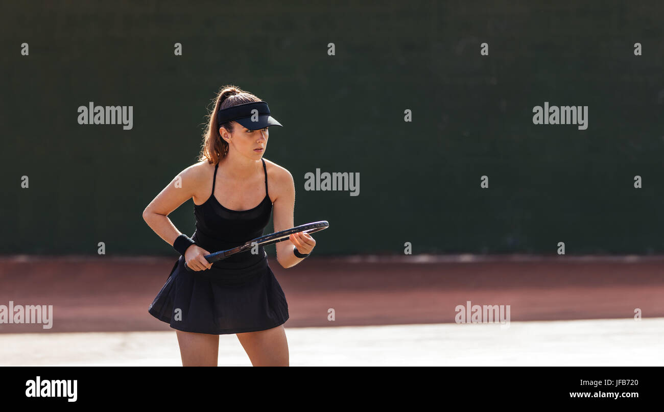 Sportswoman with racket at the tennis court. Beautiful young woman standing on outdoor court and playing a tennis match. Stock Photo
