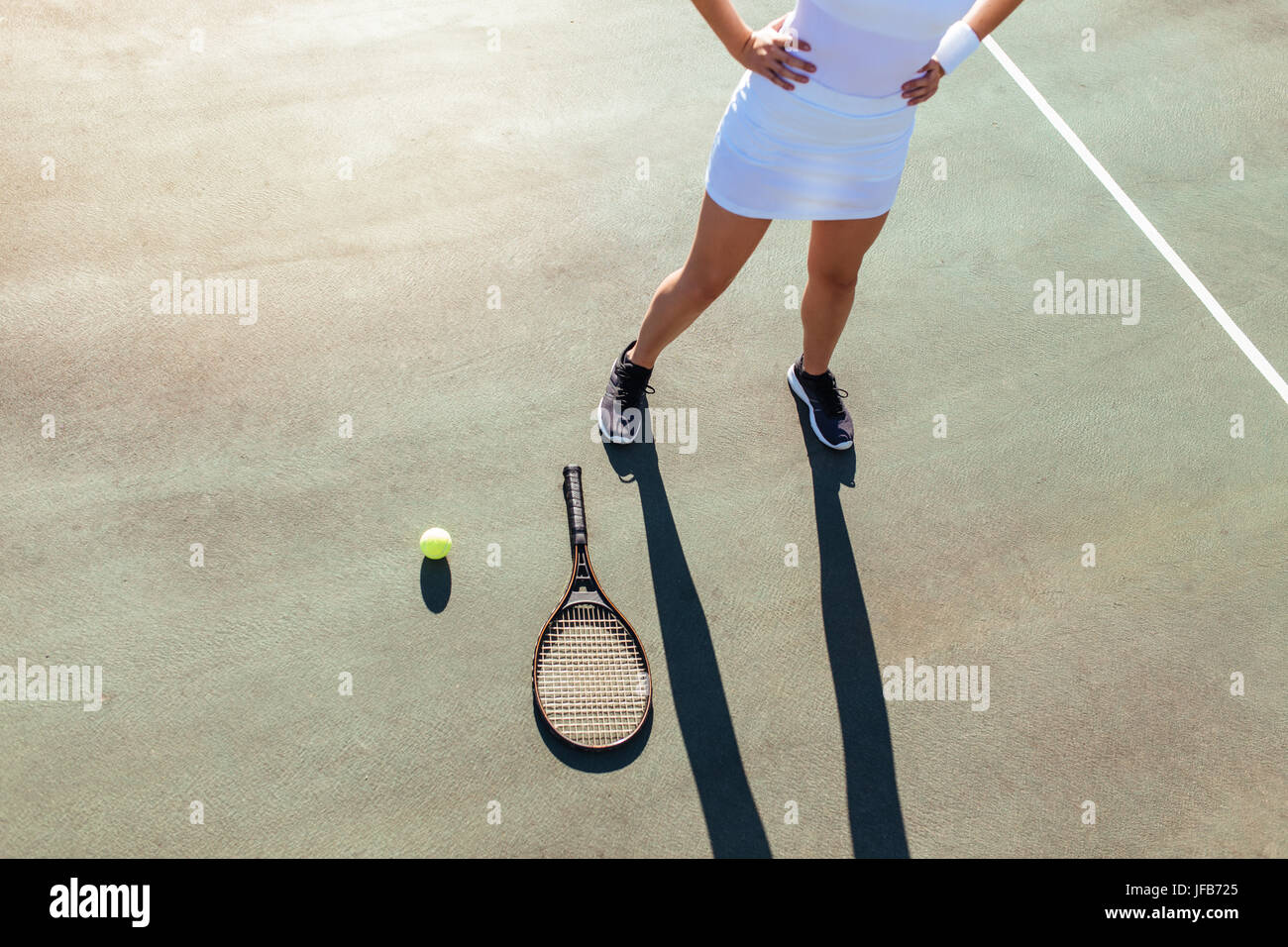 Young woman standing with racket and ball on tennis court . Sportswoman standing with hands on hips. Stock Photo