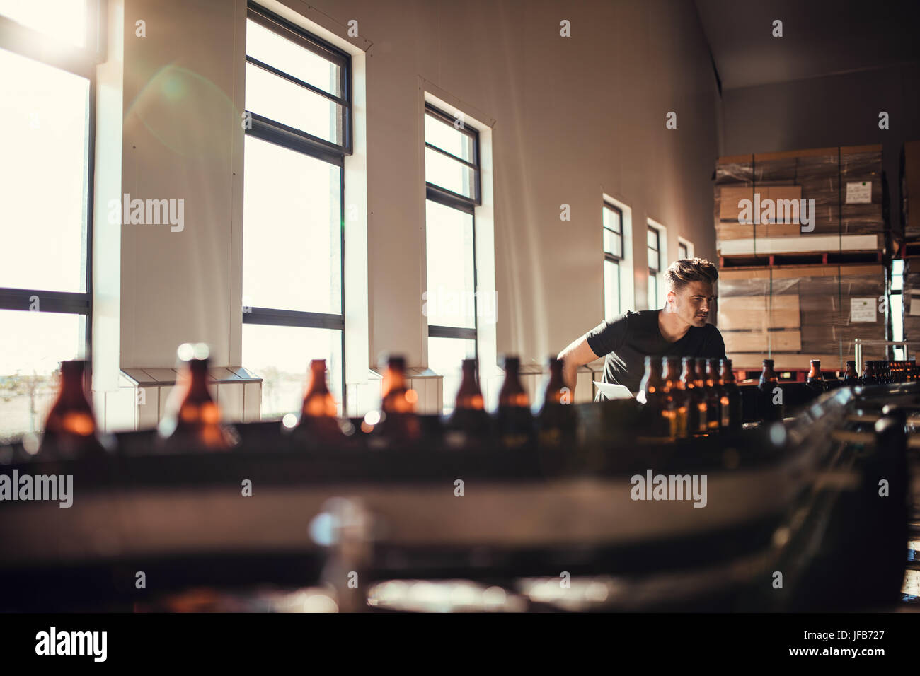 Young man supervising the production of craft beer at brewery. Man working at alcohol manufacturing factory. Stock Photo