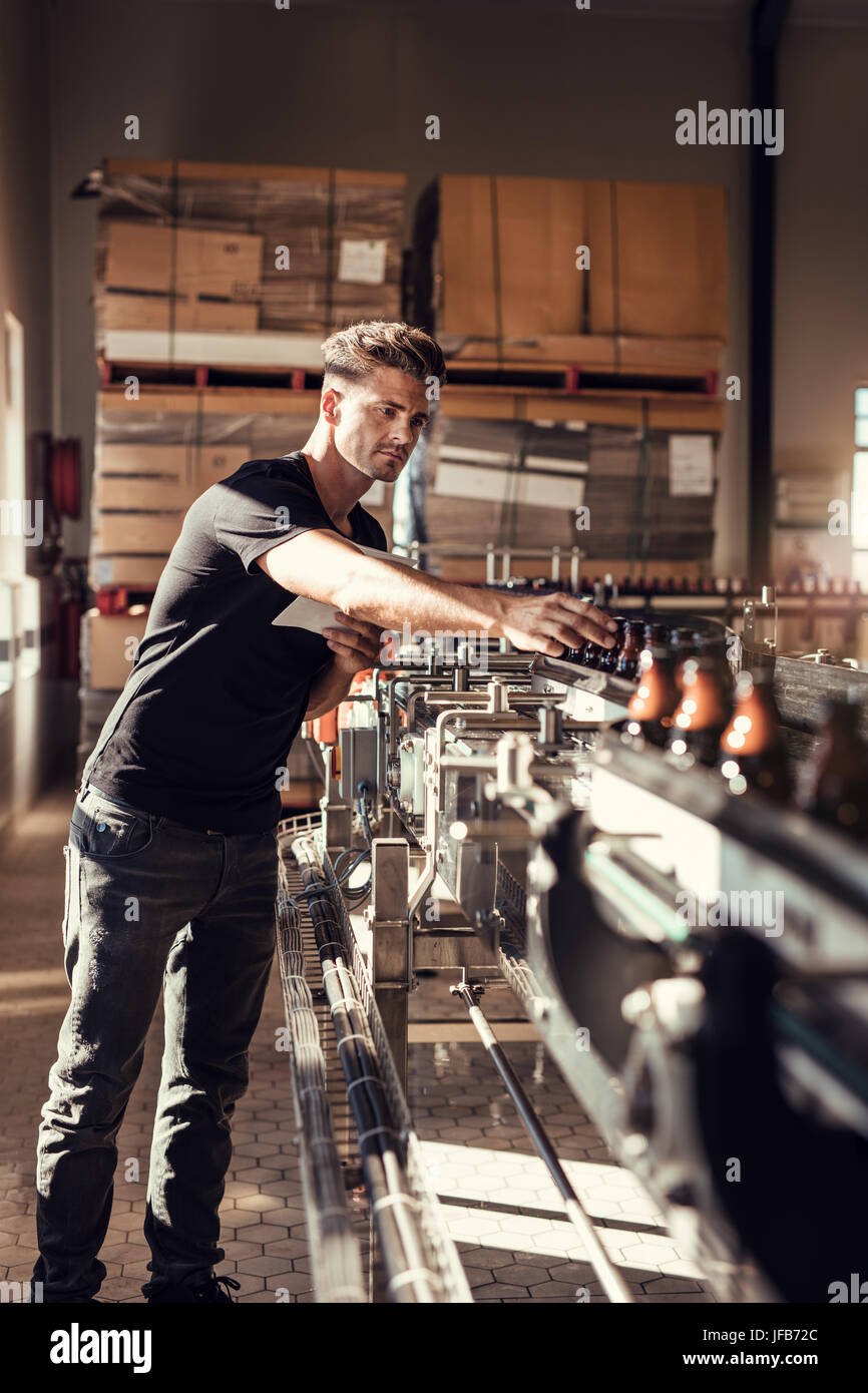 Brewer supervising the process of beer manufacturing in brewery plant. Young man at the beer bottling machine in factory. Stock Photo