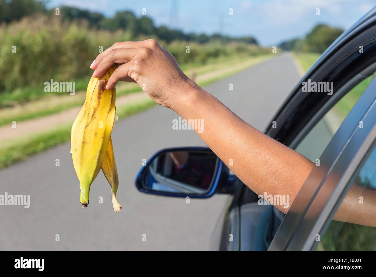 Arm dropping peel of banana out car window Stock Photo