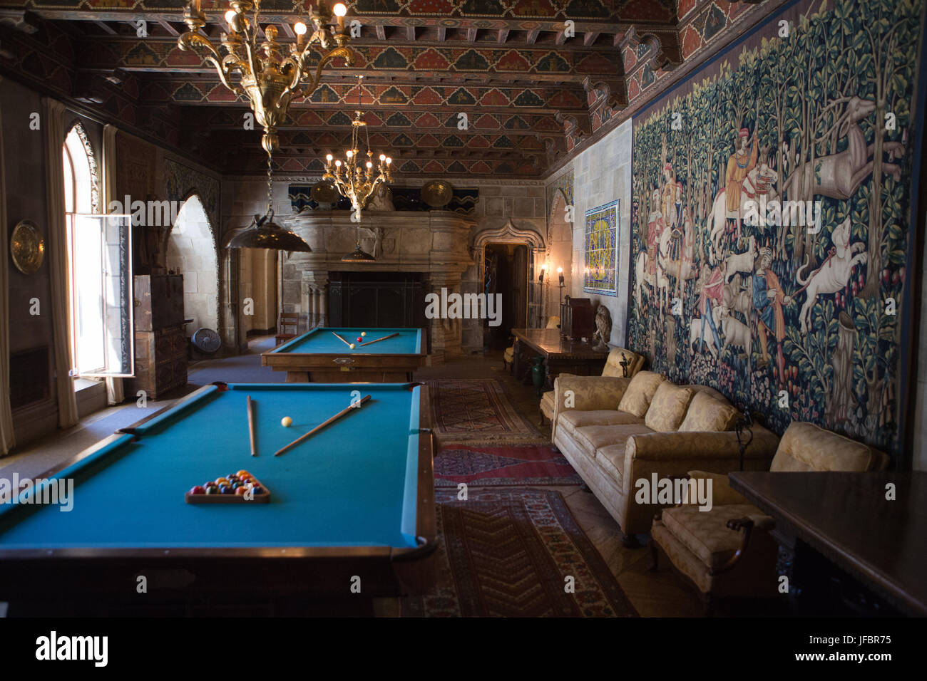 The Hearst Castle billiards room is decorated with furniture, tapestries, artwork and ornate light fixtures. Stock Photo