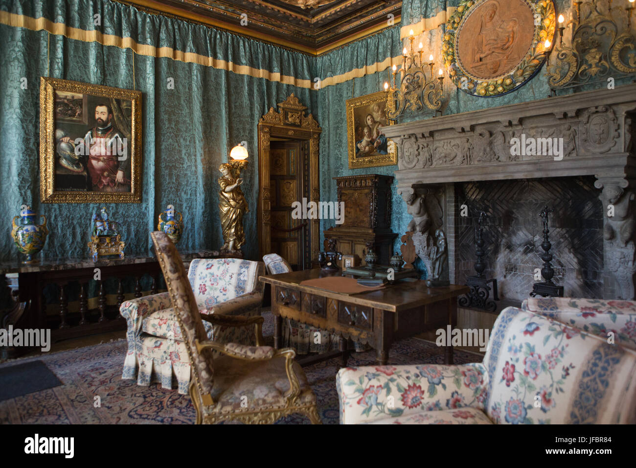 A sitting room, with a fireplace, decorated with furniture, tapestries, artwork and ornate light fixtures. Stock Photo