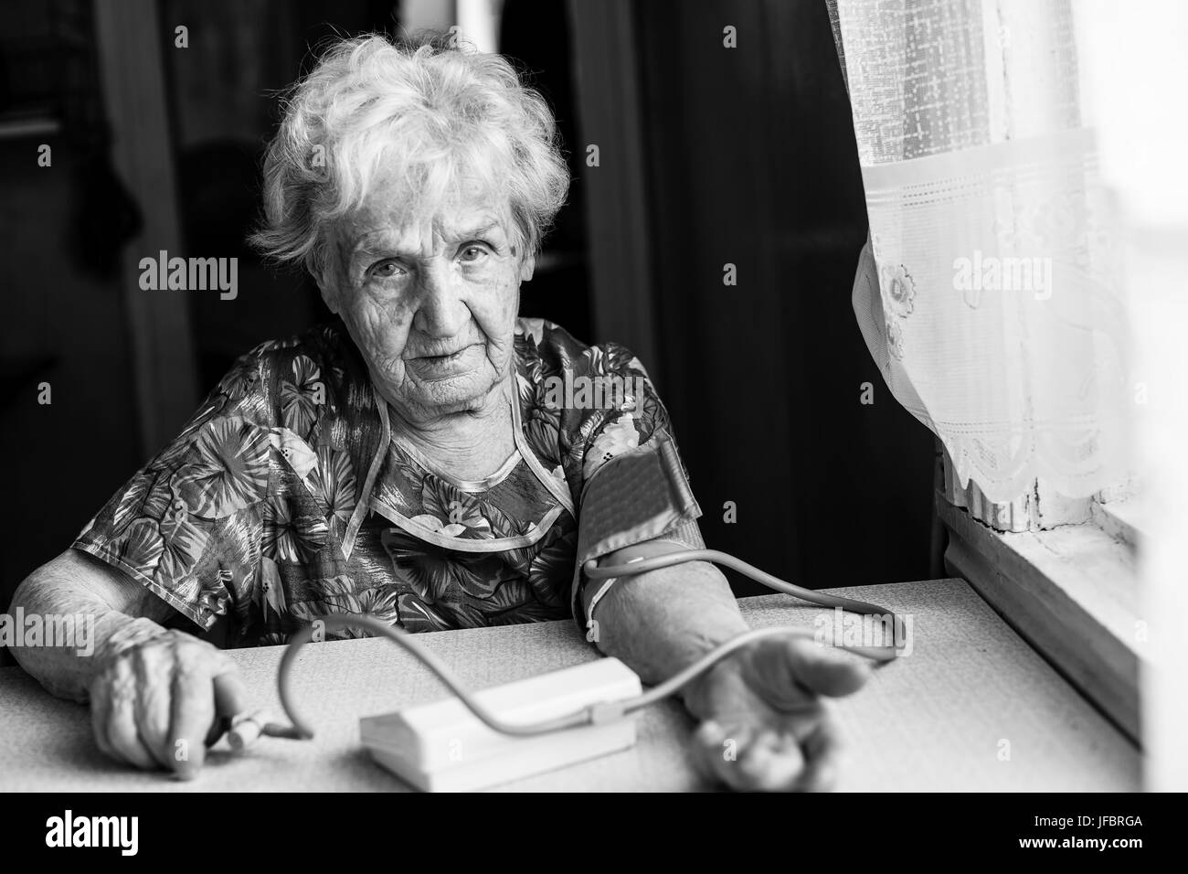 Old woman measures arterial pressure. Black-and-white photo. Stock Photo