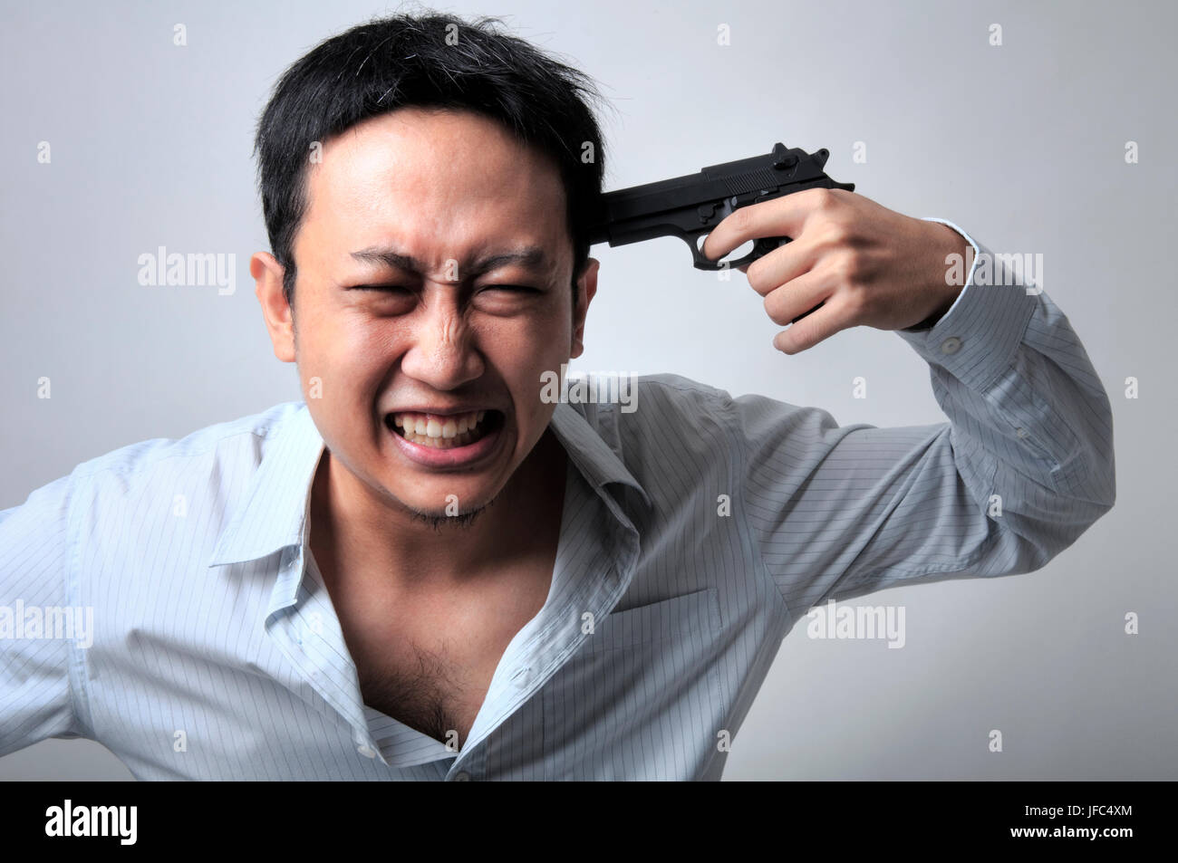 Asian businessman pointing a gun on his head, isolated on grey background. Stock Photo