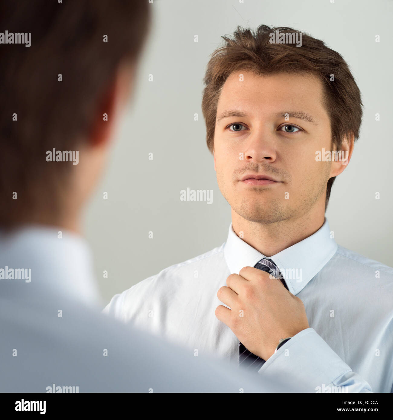 Handsome businessman preparing to official event, straighten tie. New job interview, self motivation for confidence, trying fashionable necktie knot,  Stock Photo