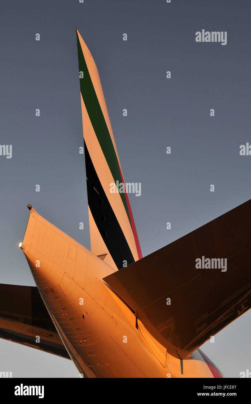The setting sun illuminates the tail of an Emirates Air, Boeing 777 stationary at an airport Stock Photo