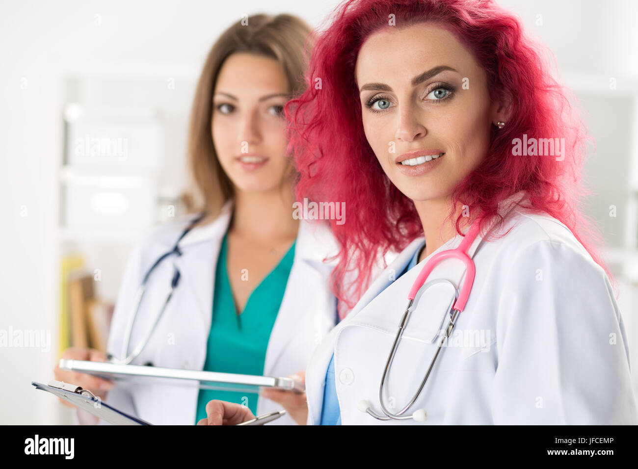 Portrait of two female doctors standing with clipboard and tablet ready to work. Health care, medical service or education and teamwork concept. Stock Photo