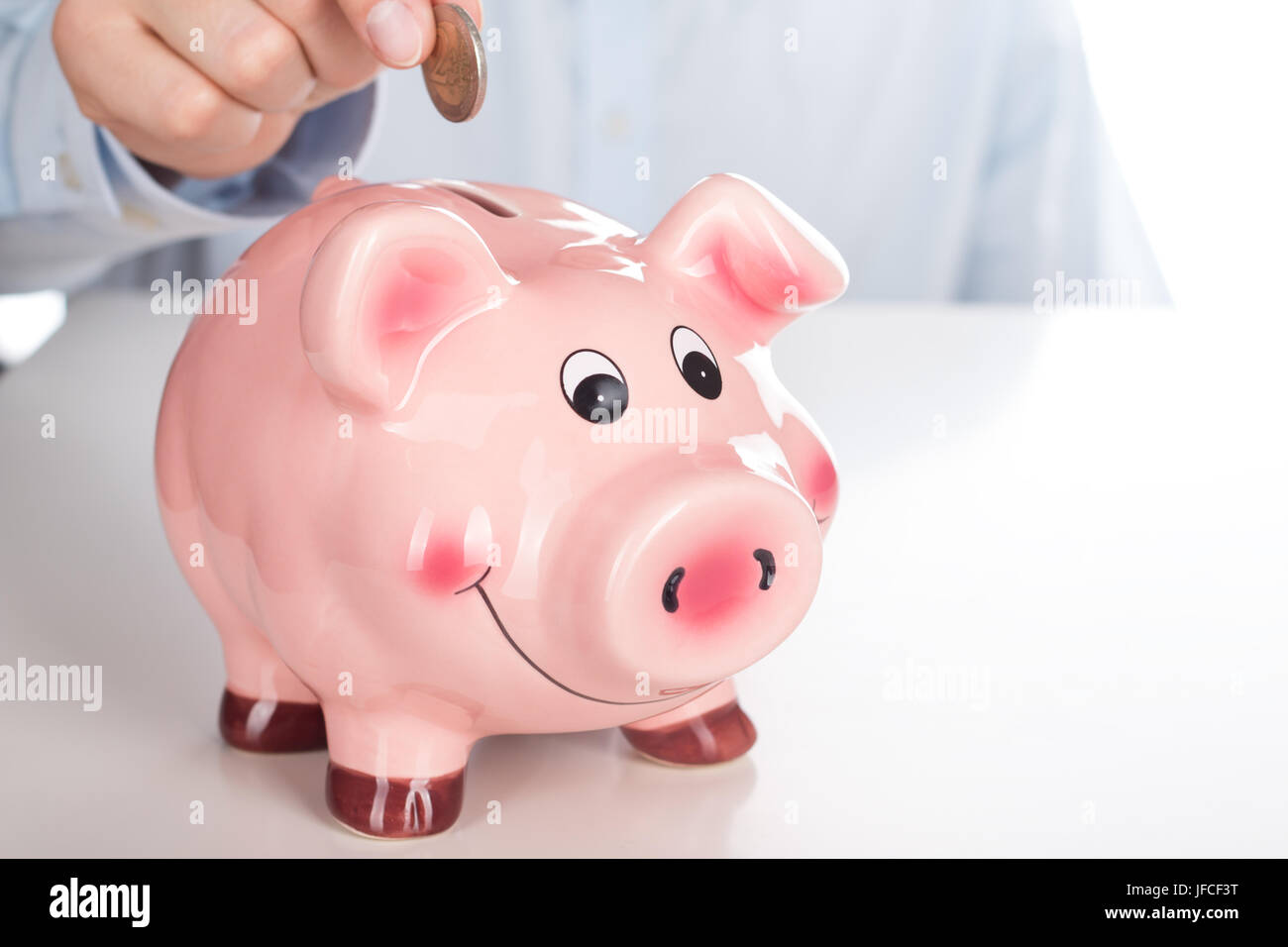 Business man hand putting coin into funny pink piggy bank. Saving money, insurance or investment concept Stock Photo
