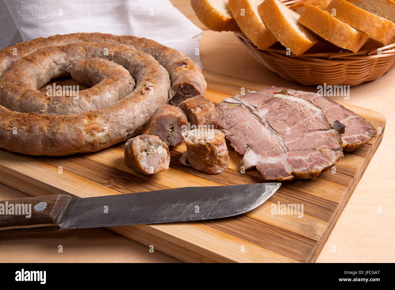 Roasted traditional homemade sausage with spices and herbs and slices spicy meat baked with herbs and spice on wooden cutting board. Slices white whea Stock Photo
