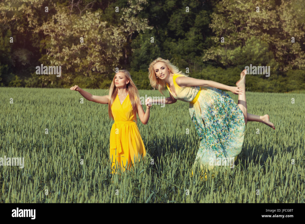 Two girls in the field. They have wore light summer dress. One girl is flying holding the hand of the second girl. Stock Photo