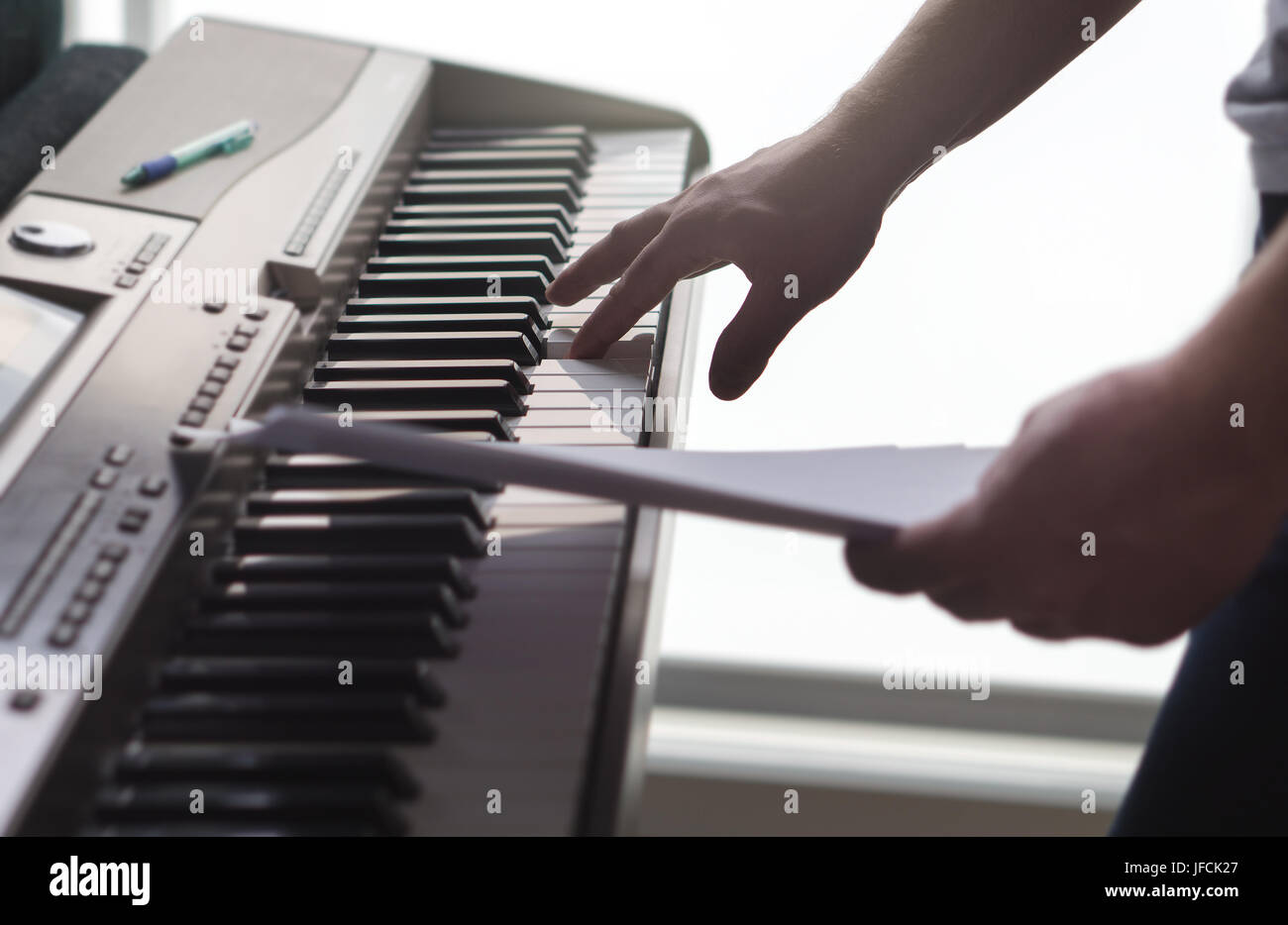 One single finger pressing key on piano. Man looking at paper notes and training a new song or melody from the sheet music. Pianist composing new work Stock Photo