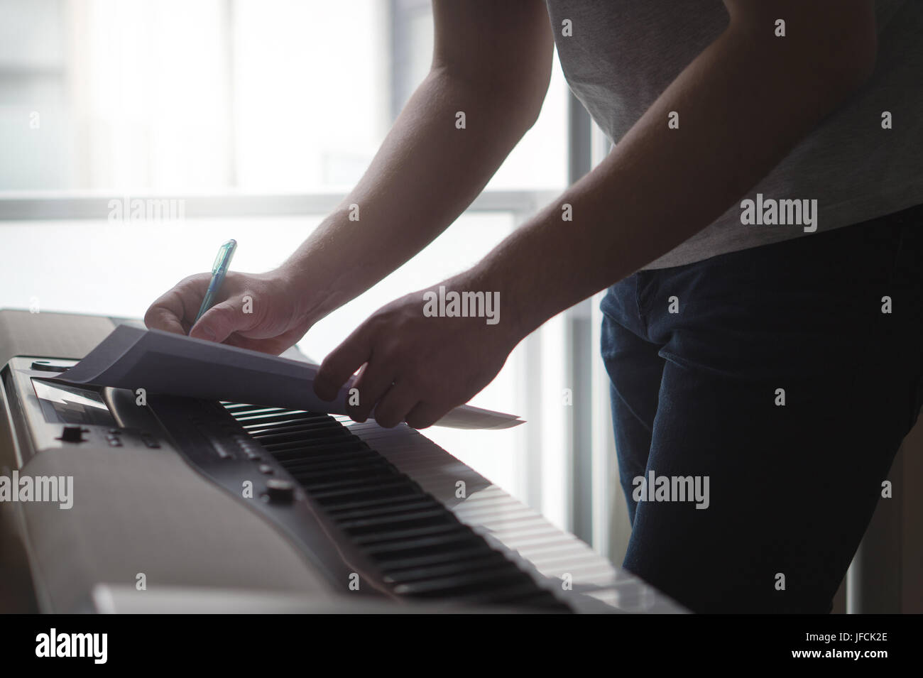 Composer and songwriter writing notes or lyrics on paper on piano. Musician write a song in home studio on an digital instrument. Stock Photo