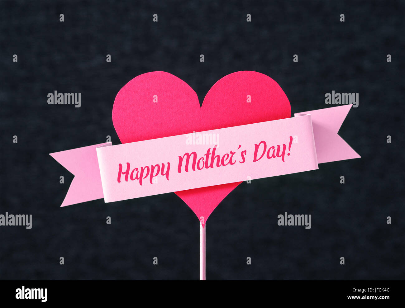 Happy Mother's Day text on a ribbon and red heart shape cut from cardboard on wooden stick. Nice simple greeting design for Mothers Day card. Stock Photo