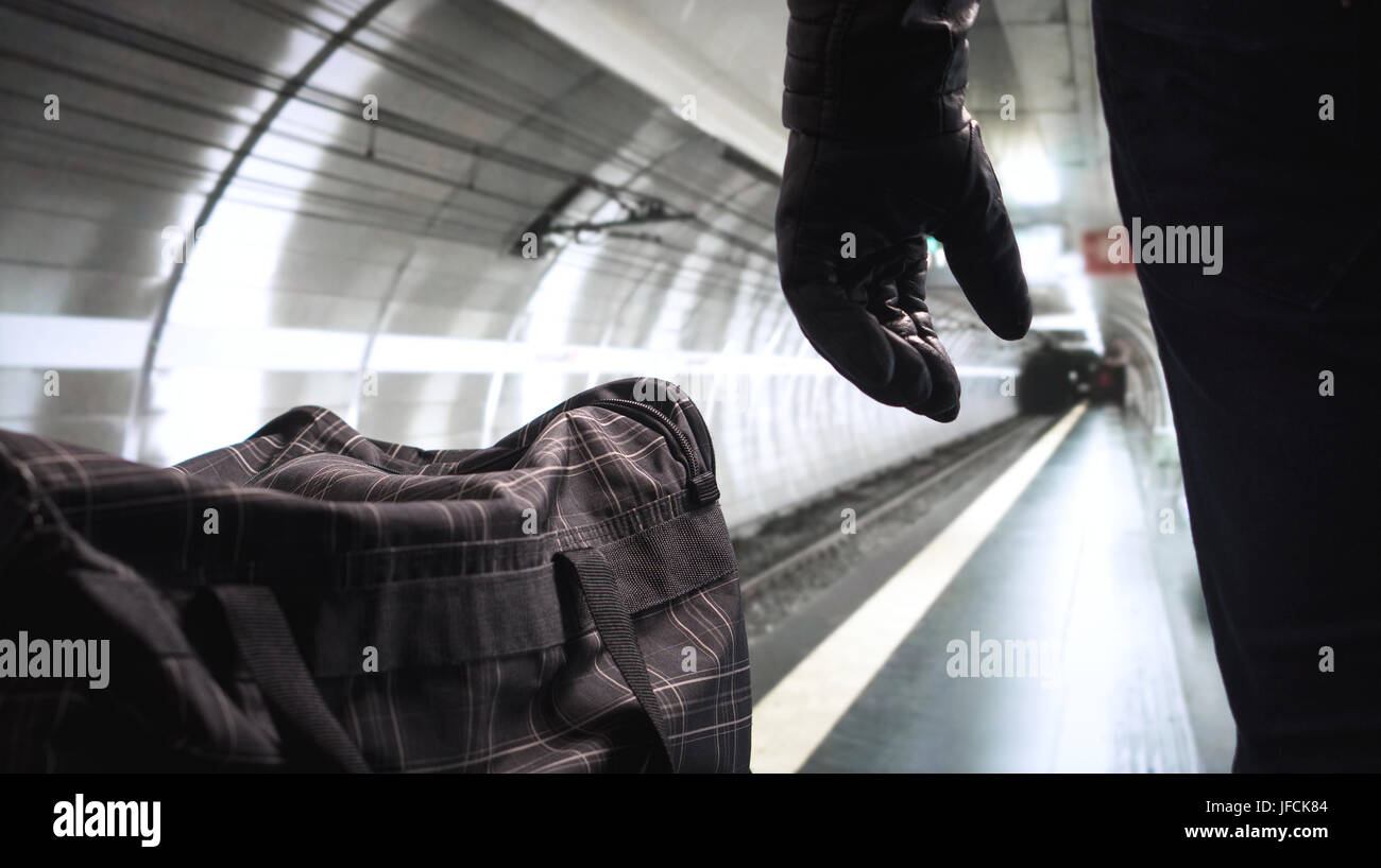 Terrorist in underground subway. Terrorism in empty metro platform. Security threat. Bomber standing next to his black bomb bag planning a strike. Stock Photo