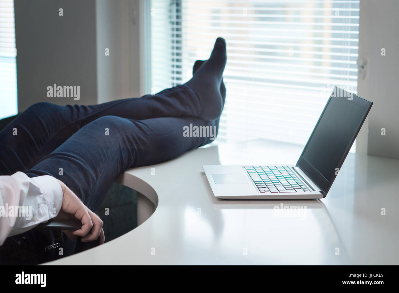 Lazy office worker with feet and socks on table. Useless and relaxing man doing nothing or taking break from work in workstation. Stock Photo
