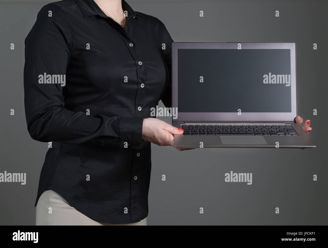 Business woman presenting a software or showing an application. Girl holding laptop with dynamic pose and black collared shirt. Empty screen. Stock Photo