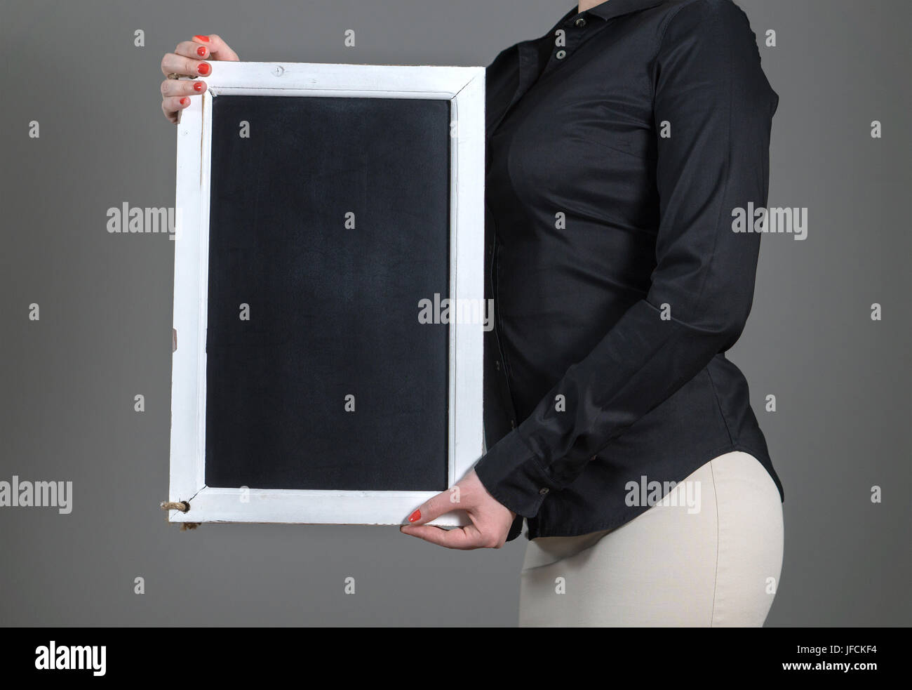 Waitress holding chalkboard vertically on a dark gray background. Free blank empty copy space for text, menu or specials. Waiter in a restaurant. Stock Photo