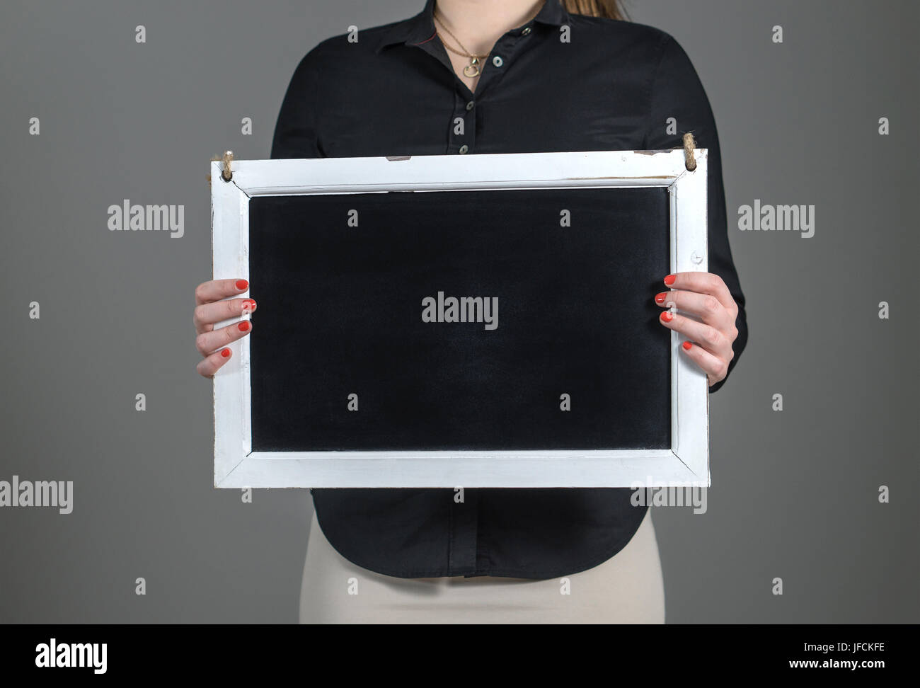 Woman holding blank chalkboard on a dark gray background. Free blank empty copy space for text. Business person or waitress in a restaurant. Stock Photo