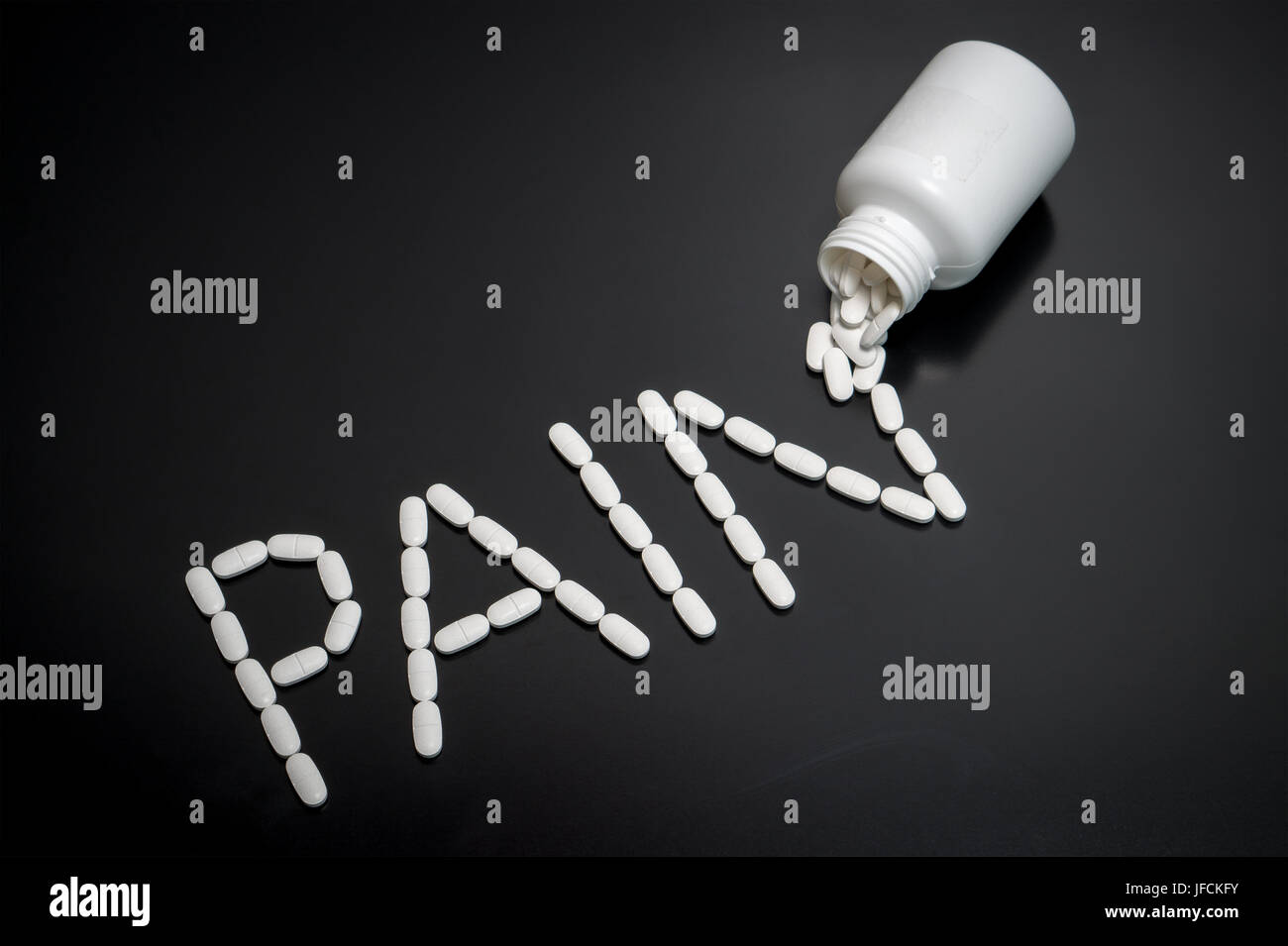 Pain killers spilling from bottle on dark table. The word pain written with medicine coming out from package. Writing made with medical products. Stock Photo